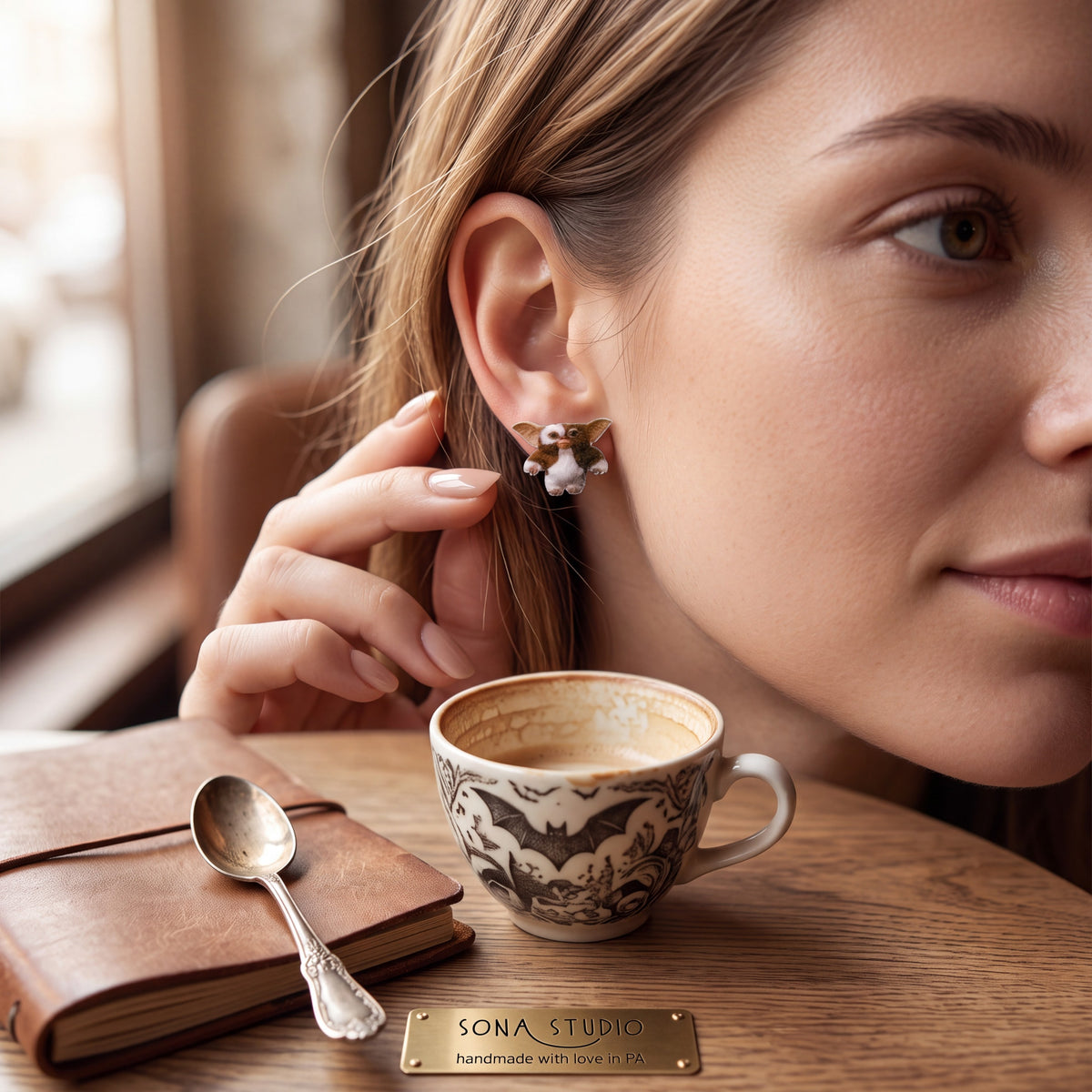 Doodlations Coffee Bar & Boutique Before Midnight earrings worn by a woman sitting at a cafe table with coffee.