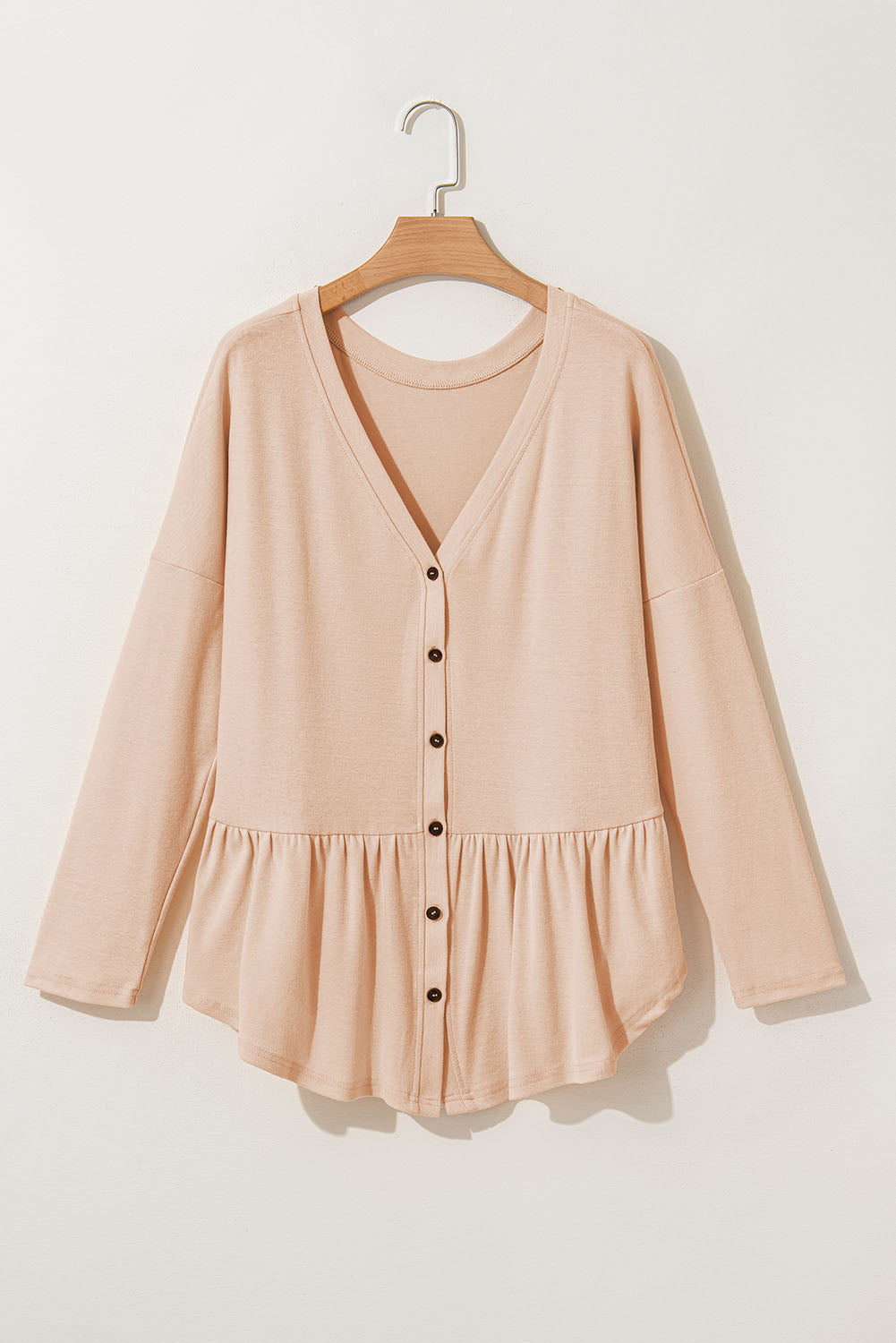Doodlations Coffee Bar & Boutique beige V-neck button-front shirt with ruffled hem detail on a wooden hanger