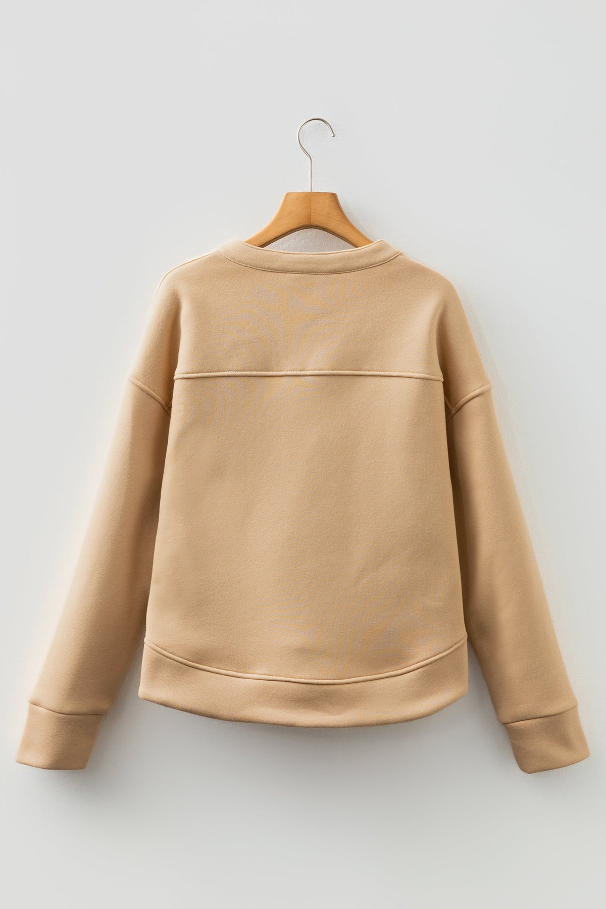 Doodlations Coffee Bar & Boutique light beige sweatshirt with a relaxed fit and back seam detail on a wooden hanger.