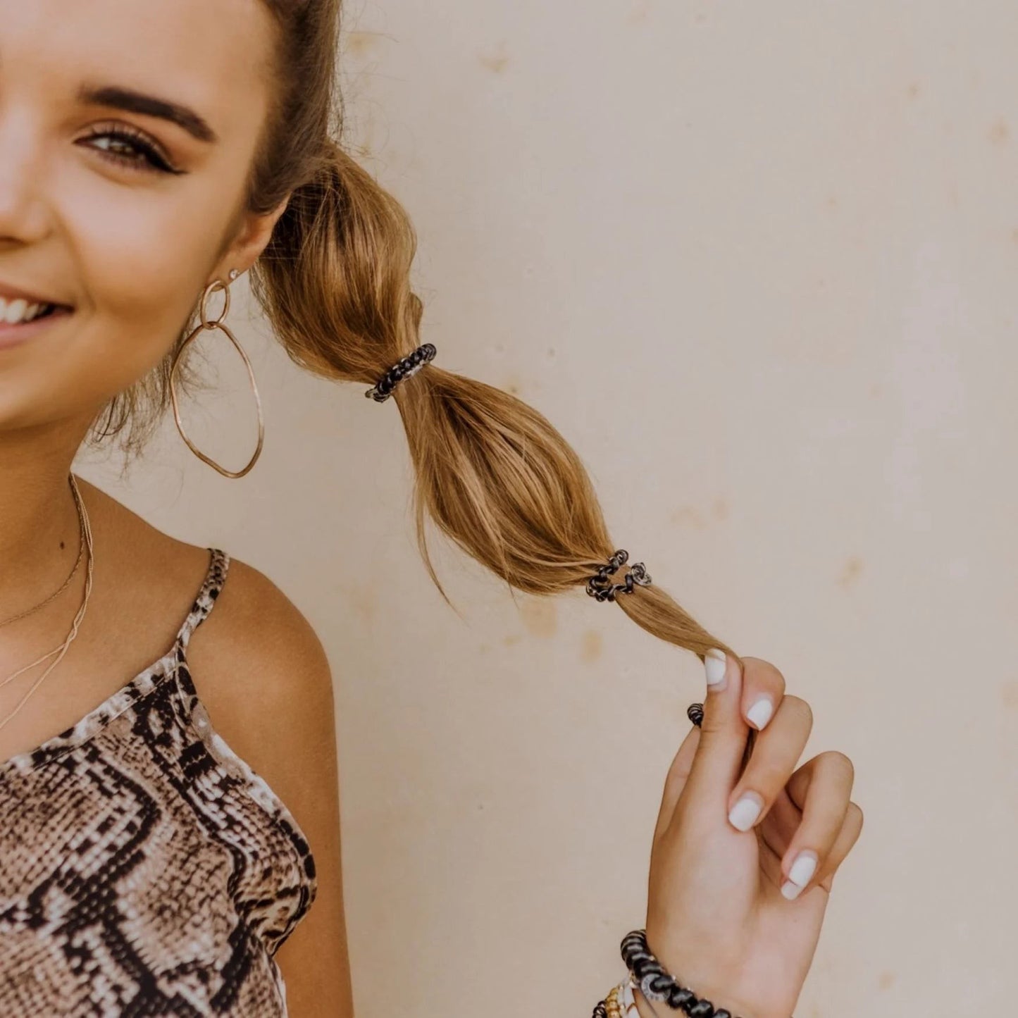 Doodlations Coffee Bar & Boutique jet black hair ties worn in a ponytail and as a bracelet on a smiling woman