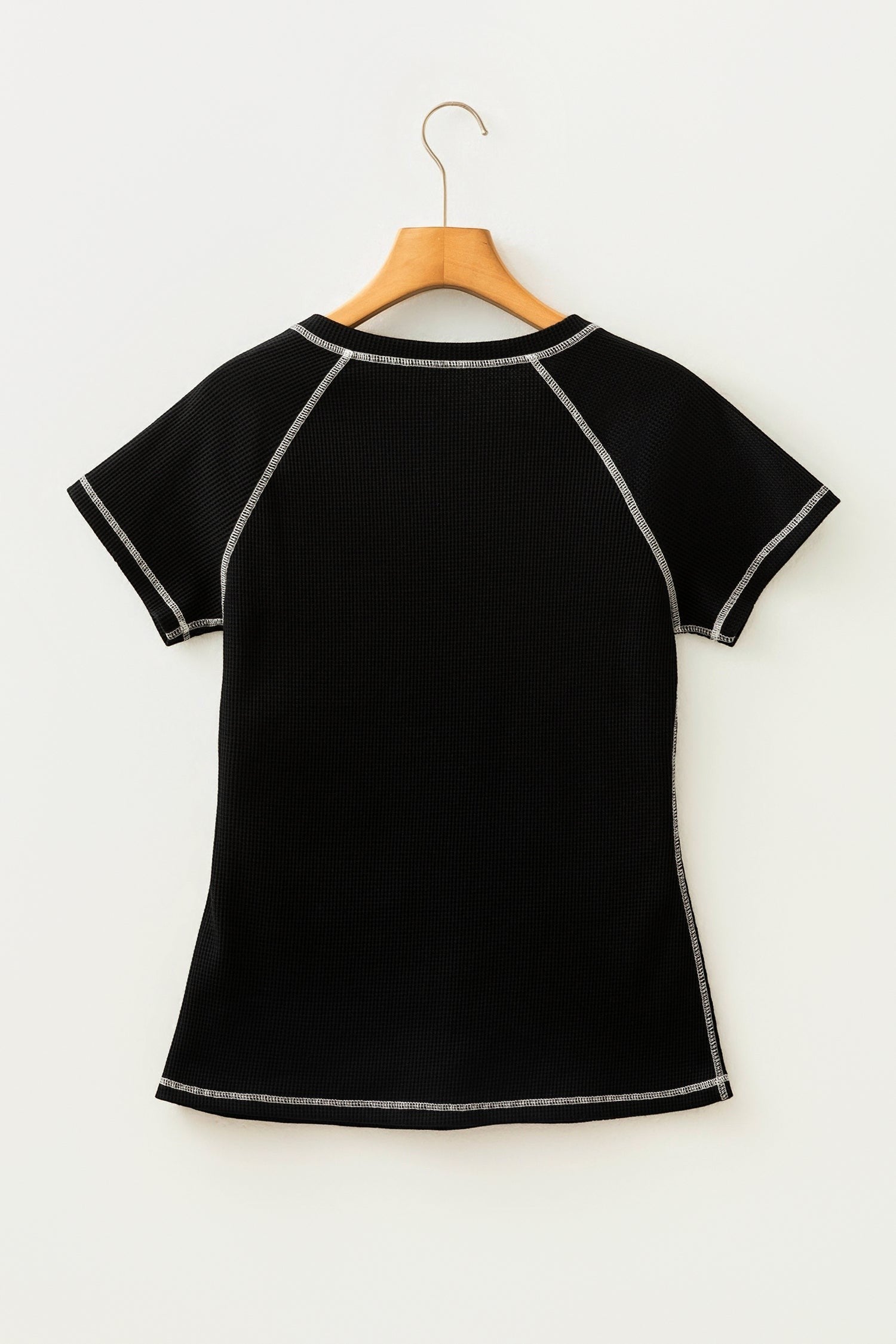 Back view of a Doodlations Coffee Bar & Boutique black waffle knit top with white contrast stitching on a hanger.