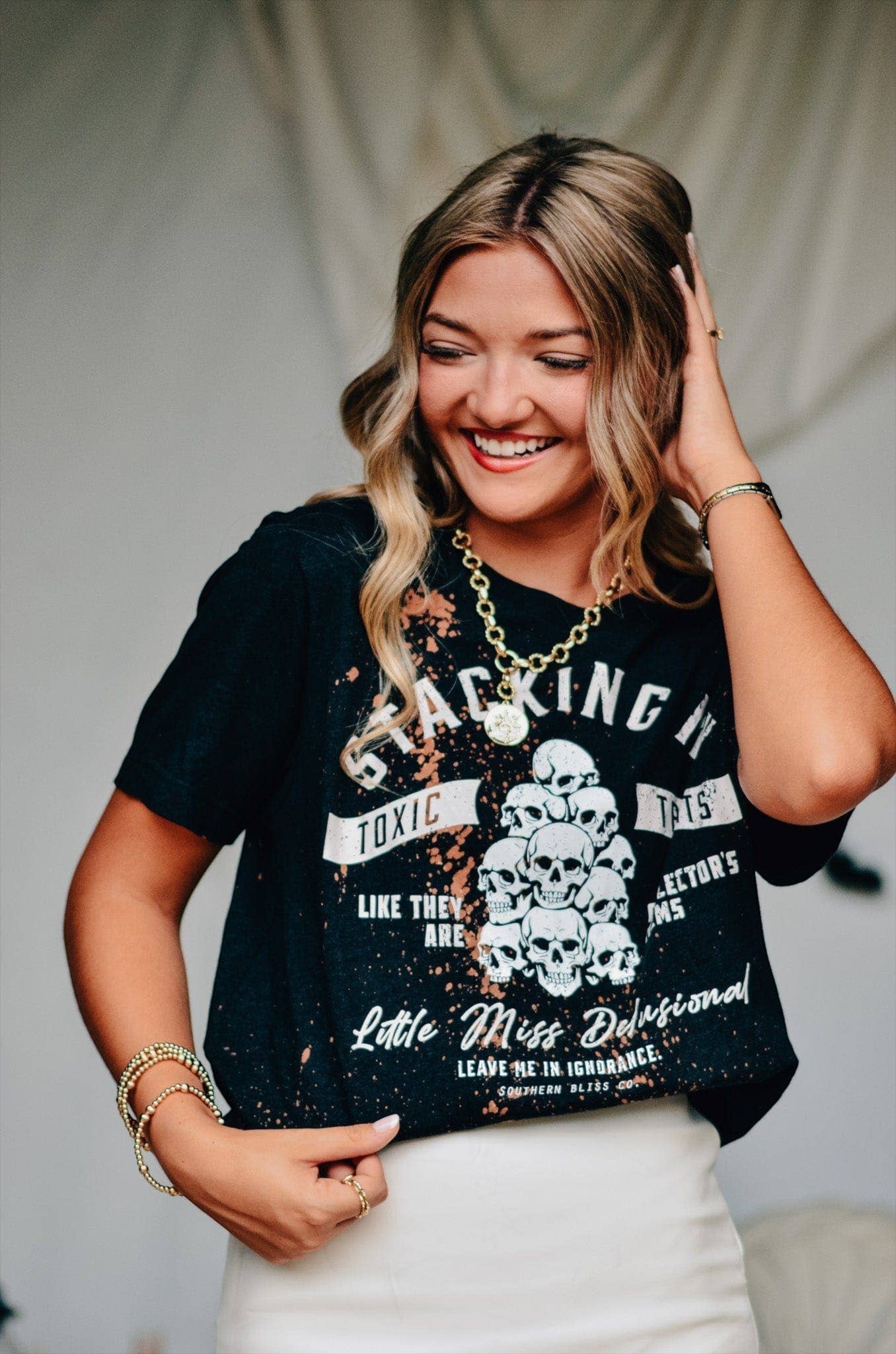 Doodlations Coffee Bar & Boutique black bleached graphic tee with skull print and sassy text worn by a smiling woman.