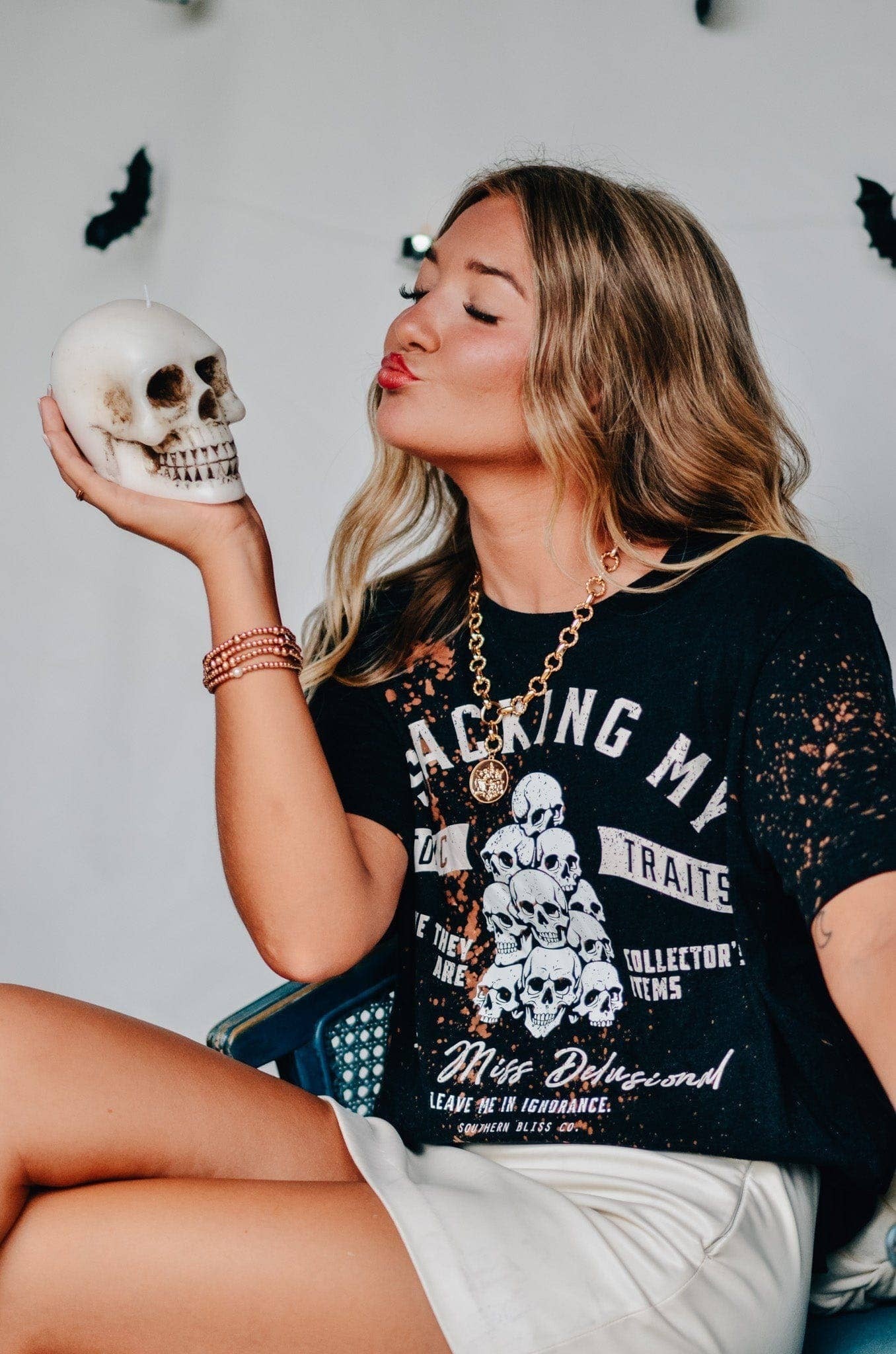 Doodlations Coffee Bar & Boutique black bleached graphic tee with skull print worn by a woman holding a skull candle
