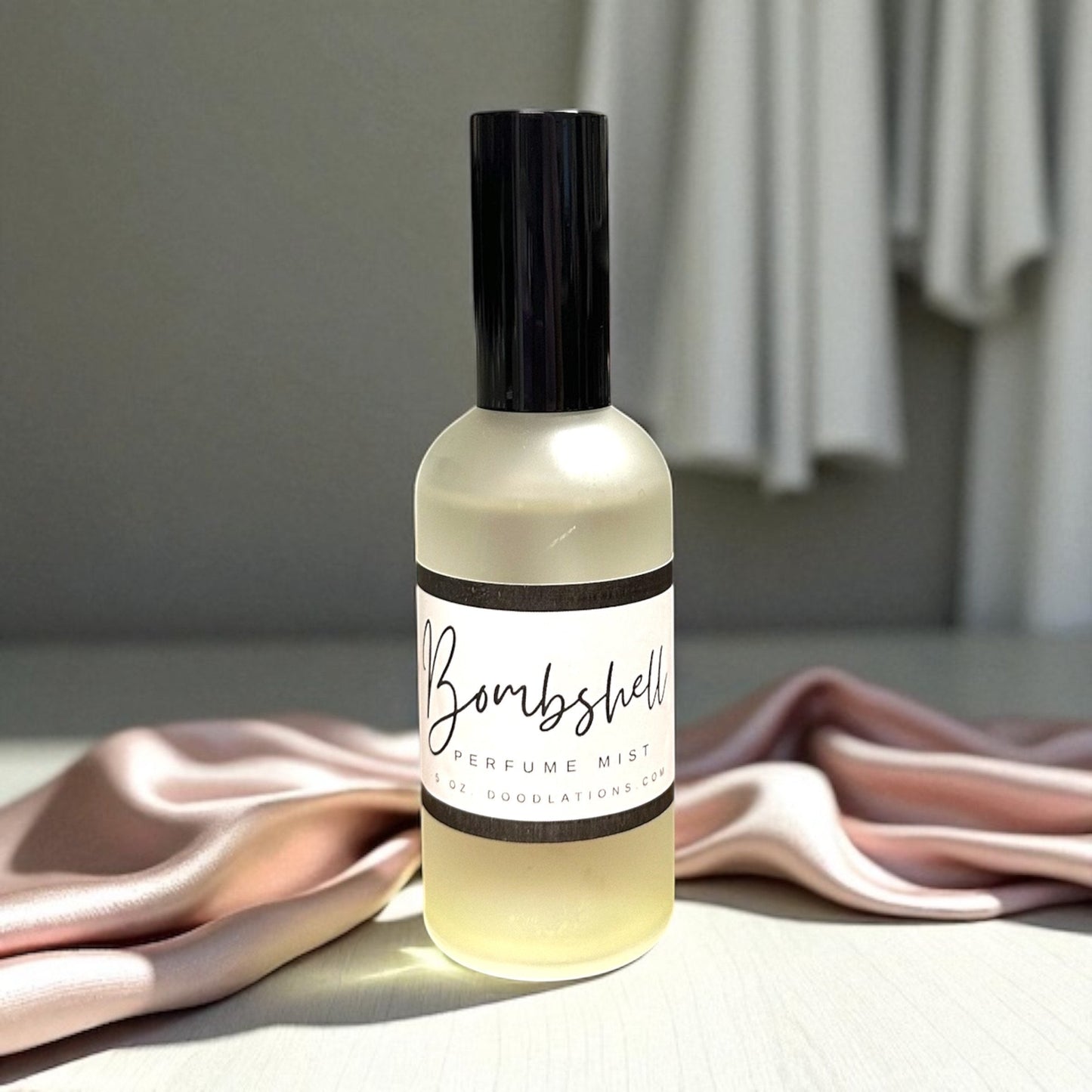 Doodlations Coffee Bar & Boutique Bombshell luxury fine mist perfume in a frosted glass bottle on soft pink fabric.