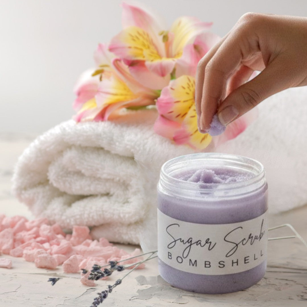 Doodlations Coffee Bar & Boutique Bombshell Sugar Scrub in a clear jar, with lavender sprigs and a lit candle.