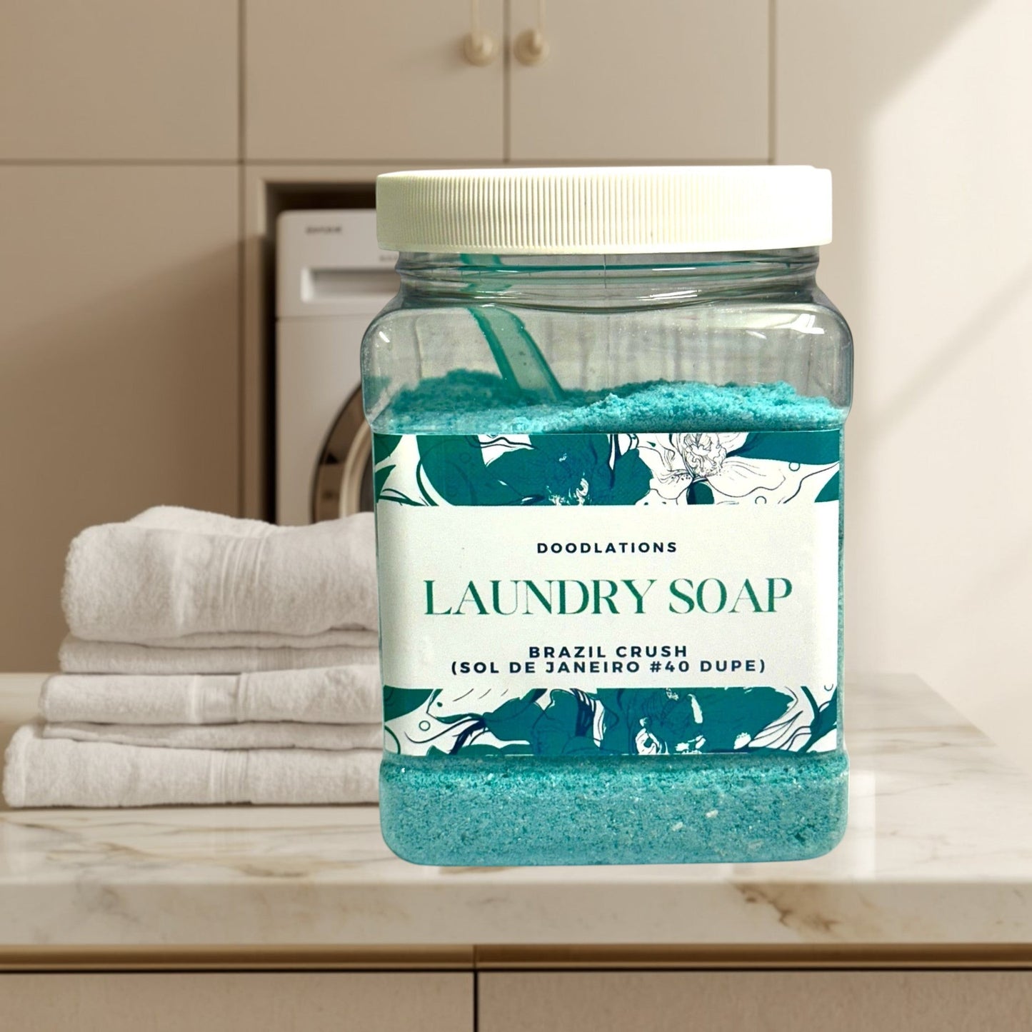 Doodlations Coffee Bar & Boutique Brazil Crush luxury laundry soap powder in a clear jar with a scoop. Teal powder with floral label.