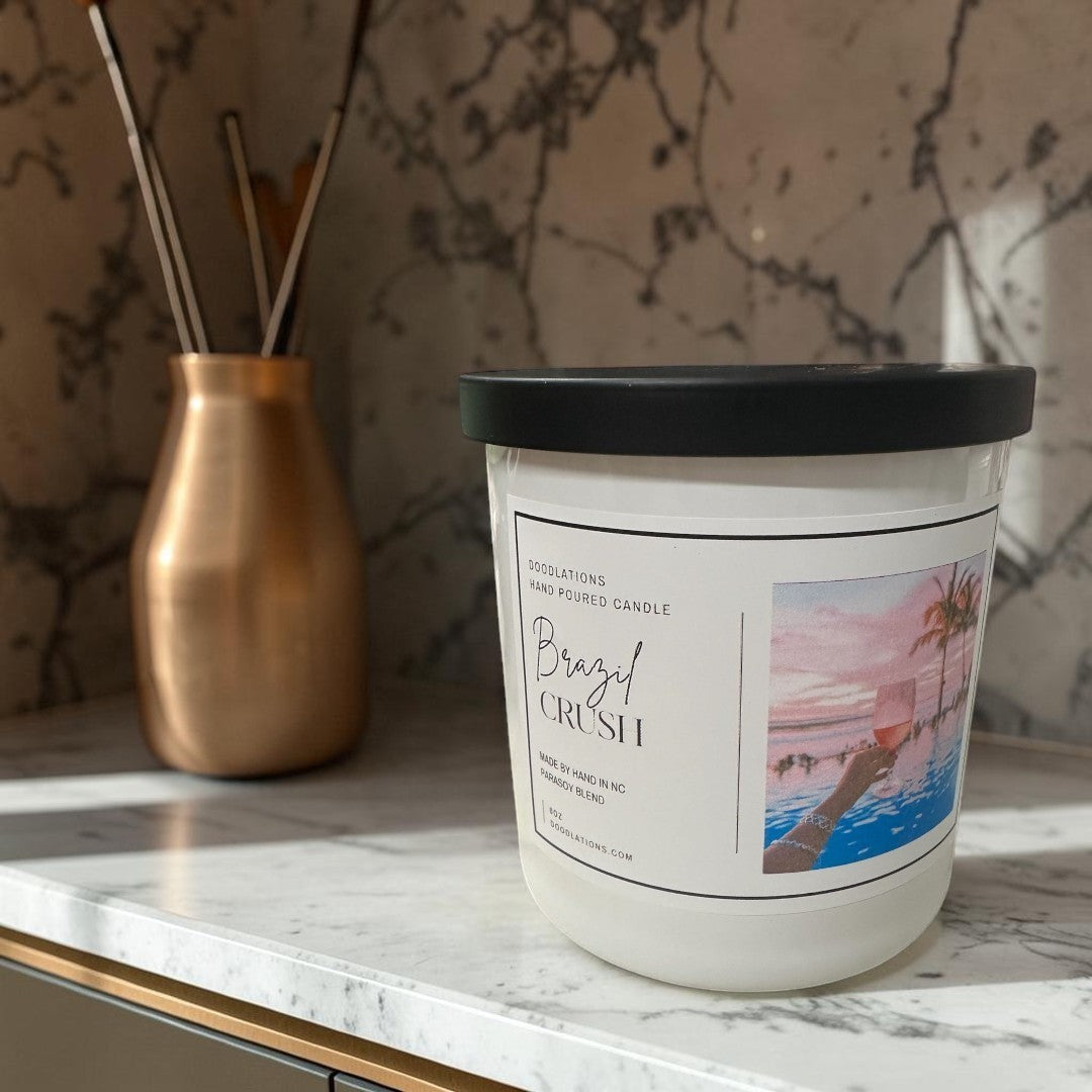 Doodlations Coffee Bar & Boutique Brazilian Crush hand-poured soy blend candle with a tropical sunset label.