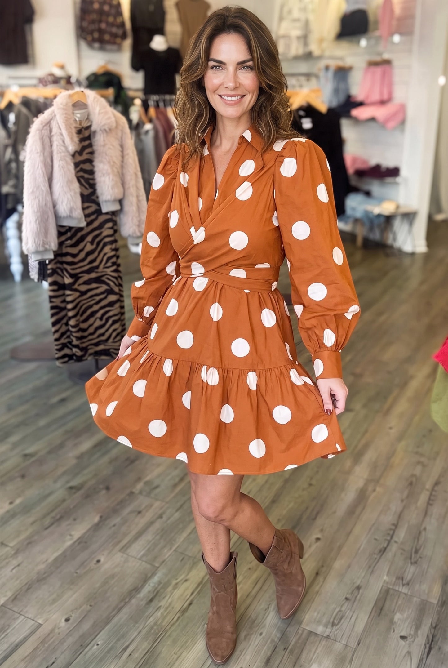 A woman wearing a Doodlations Coffee Bar & Boutique brown polka dot long sleeve mini dress with a tie waist.