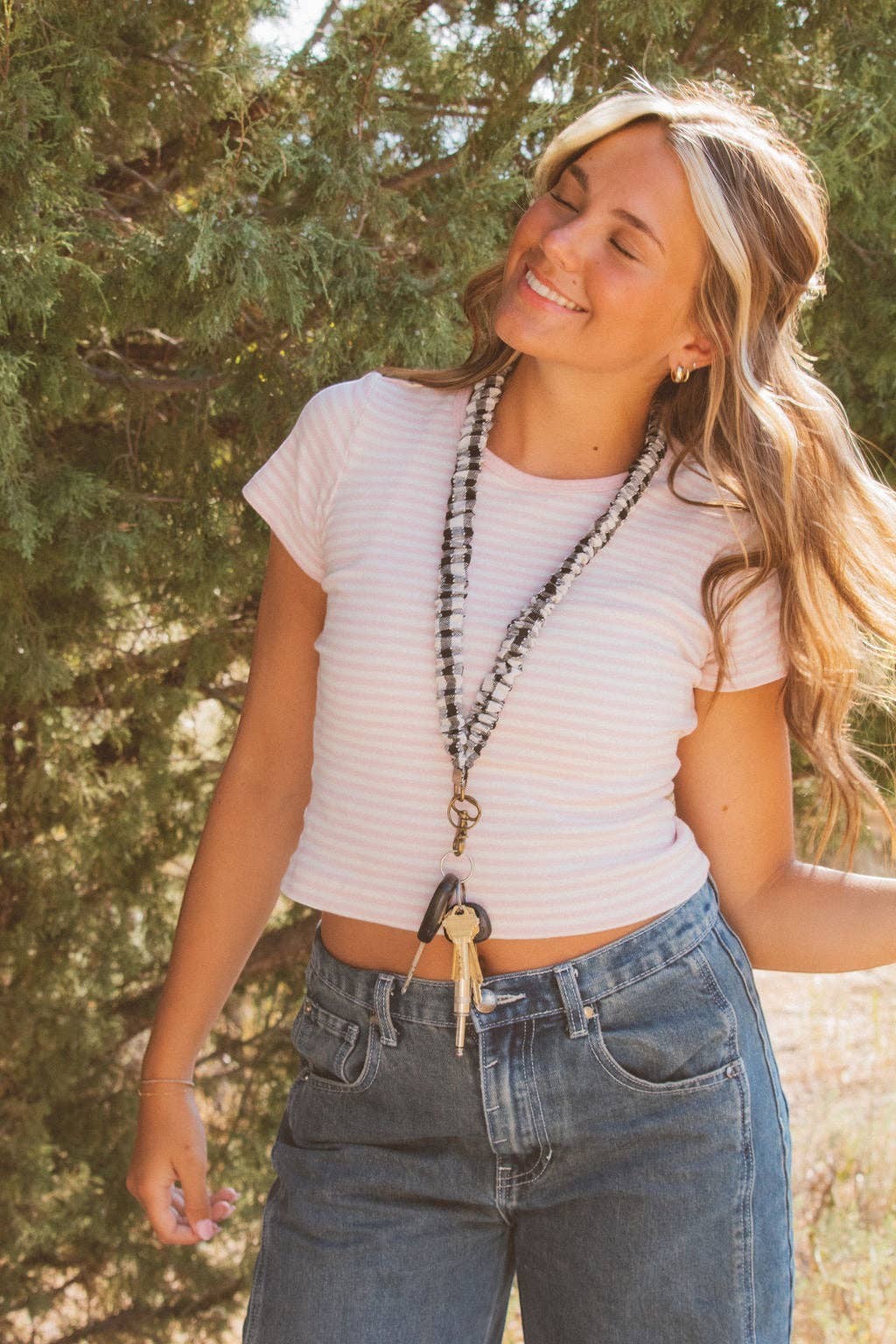 Doodlations Coffee Bar & Boutique black and white buffalo check fabric lanyard worn by a smiling woman outdoors