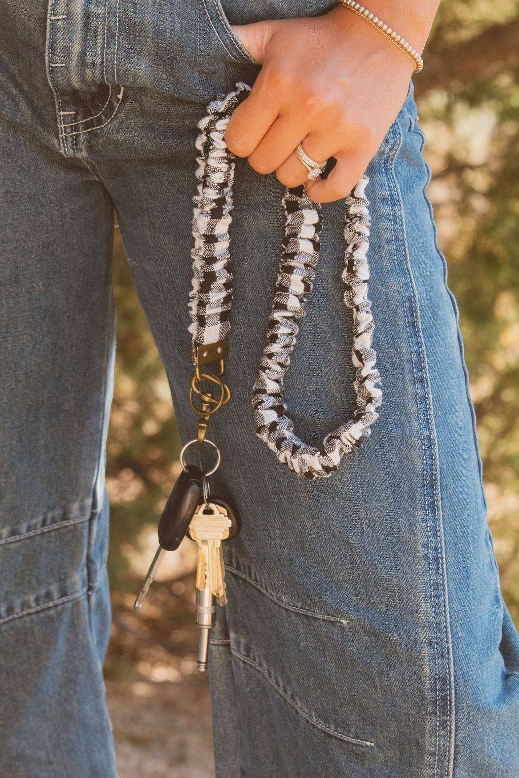 Doodlations Coffee Bar & Boutique black and white buffalo check fabric lanyard with keys held by a person in jeans.