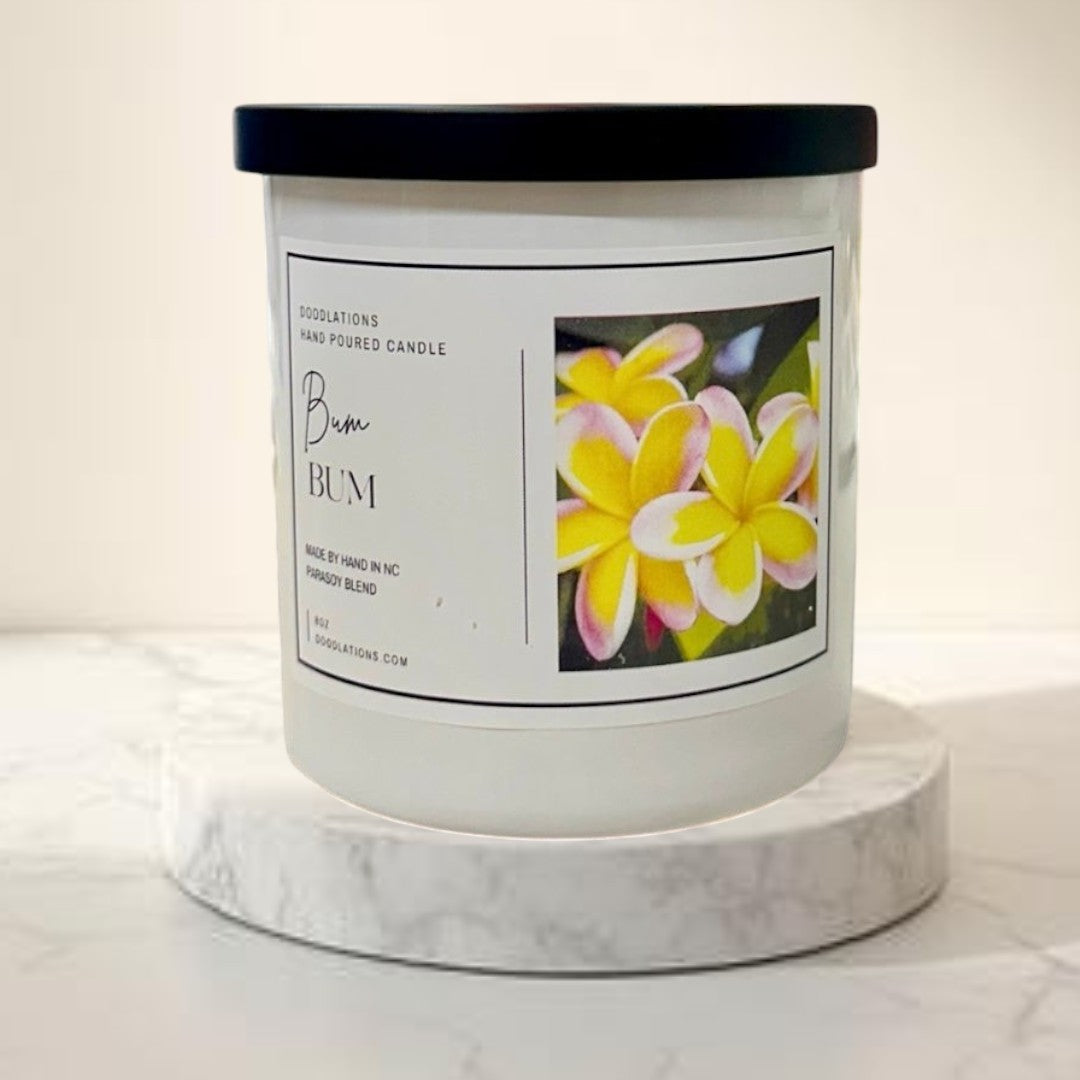 Doodlations Coffee Bar & Boutique Bum Bum luxury candle, white jar with black lid, tropical floral label, hand-poured soy blend.
