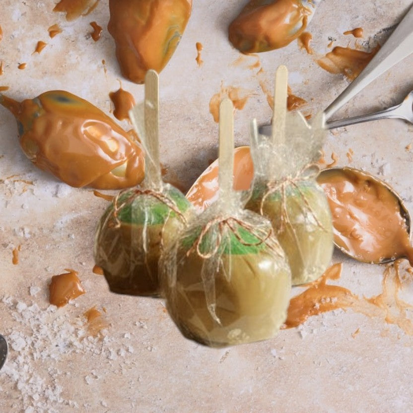 Three caramel apples with green tops and wooden sticks, wrapped in clear plastic and tied with twine, from Doodlations Coffee Bar & Boutique.