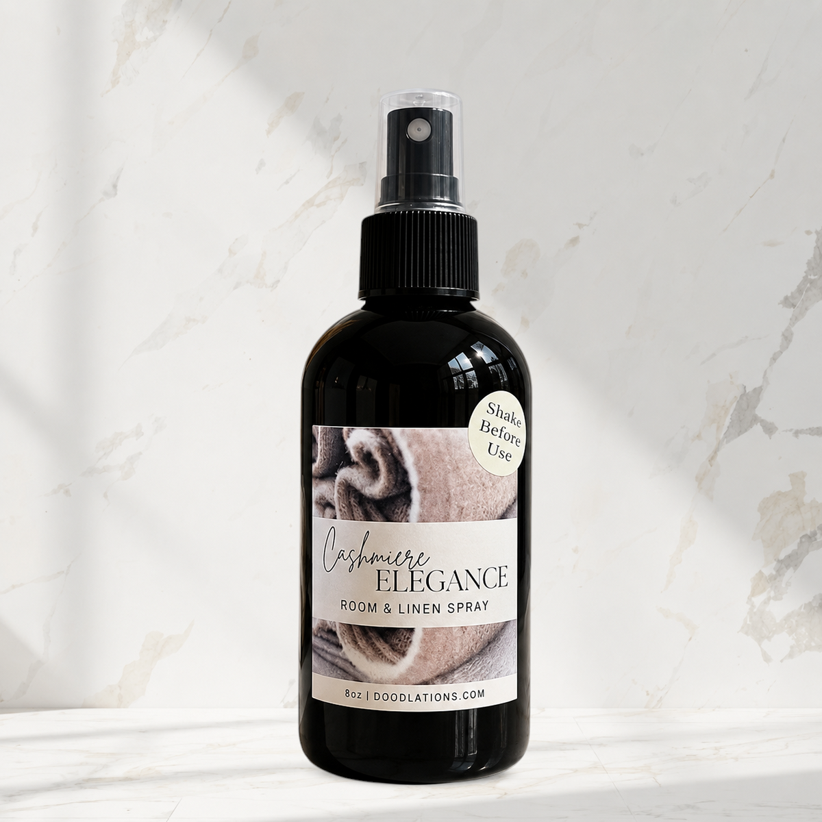 Doodlations Coffee Bar & Boutique Cashmere Elegance room and linen spray in a black bottle on a marble surface.