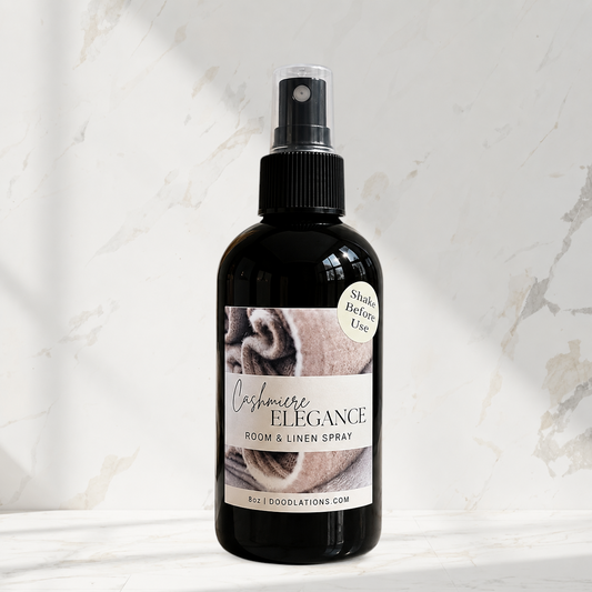 Doodlations Coffee Bar & Boutique Cashmere Elegance room and linen spray in a black bottle on a marble surface.