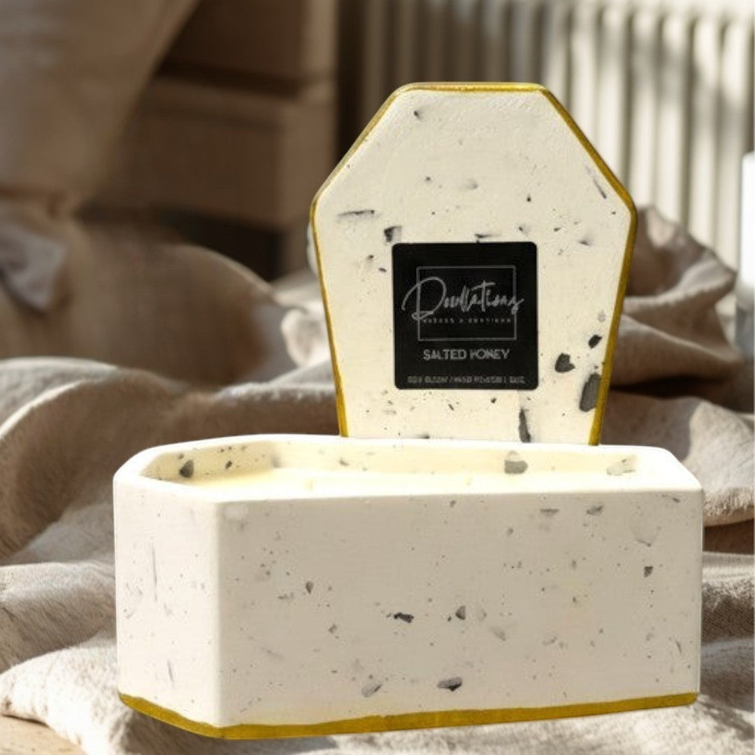 Doodlations Coffee Bar & Boutique casket-shaped concrete candle with two wicks, filled with pale yellow soy blend wax and a gold rim.