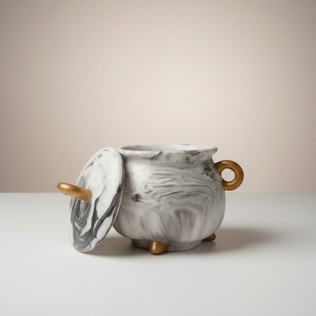 Doodlations Coffee Bar & Boutique cauldron concrete candle with gold accents and lid, marbled grey and white design.