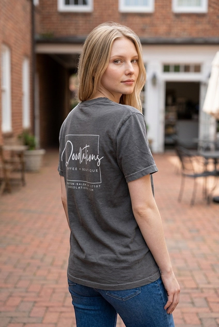 Woman wearing a charcoal grey Doodlations Coffee Bar & Boutique graphic tee with a white logo on the back