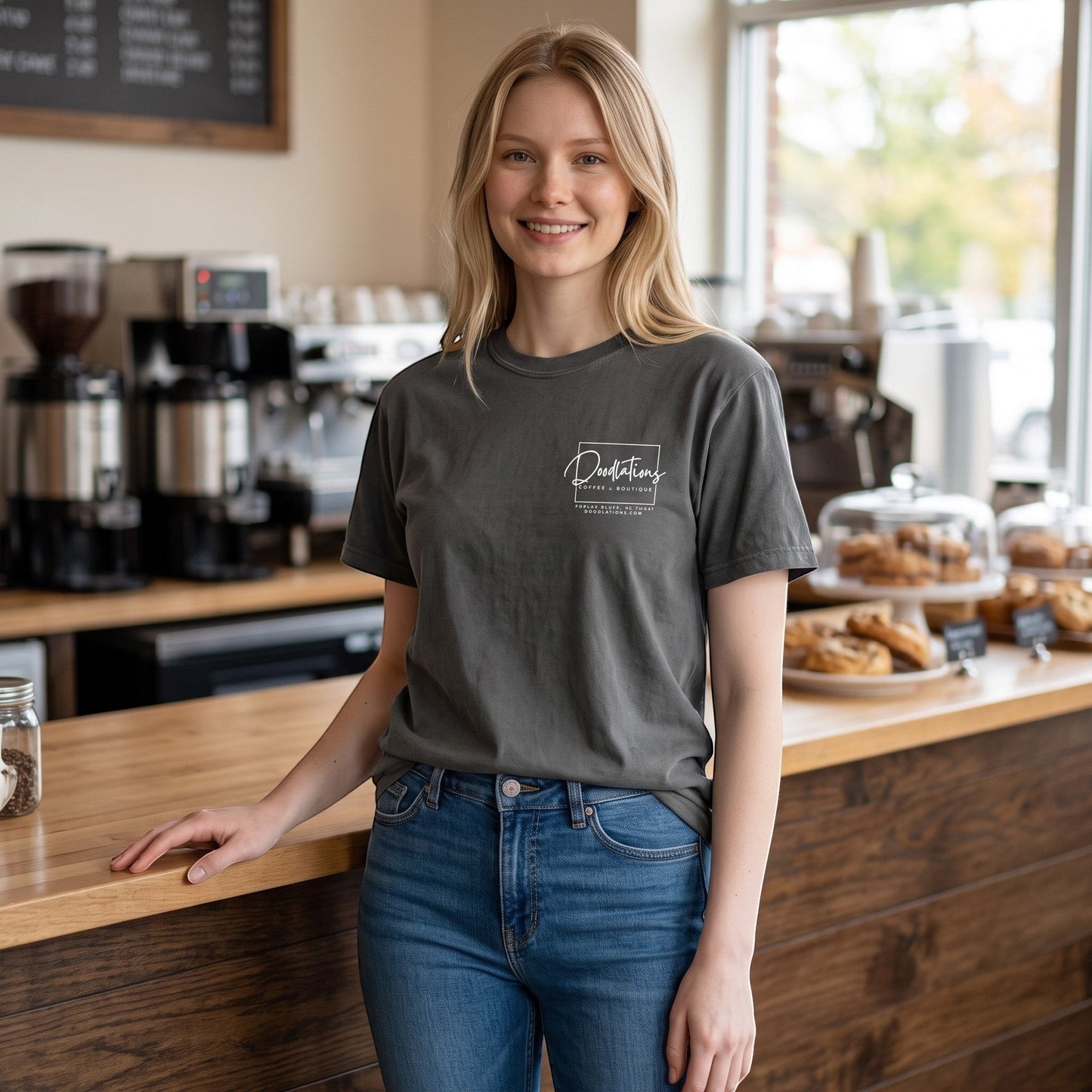 Woman wearing a charcoal grey Doodlations Coffee Bar & Boutique graphic tee with a white logo in a coffee shop