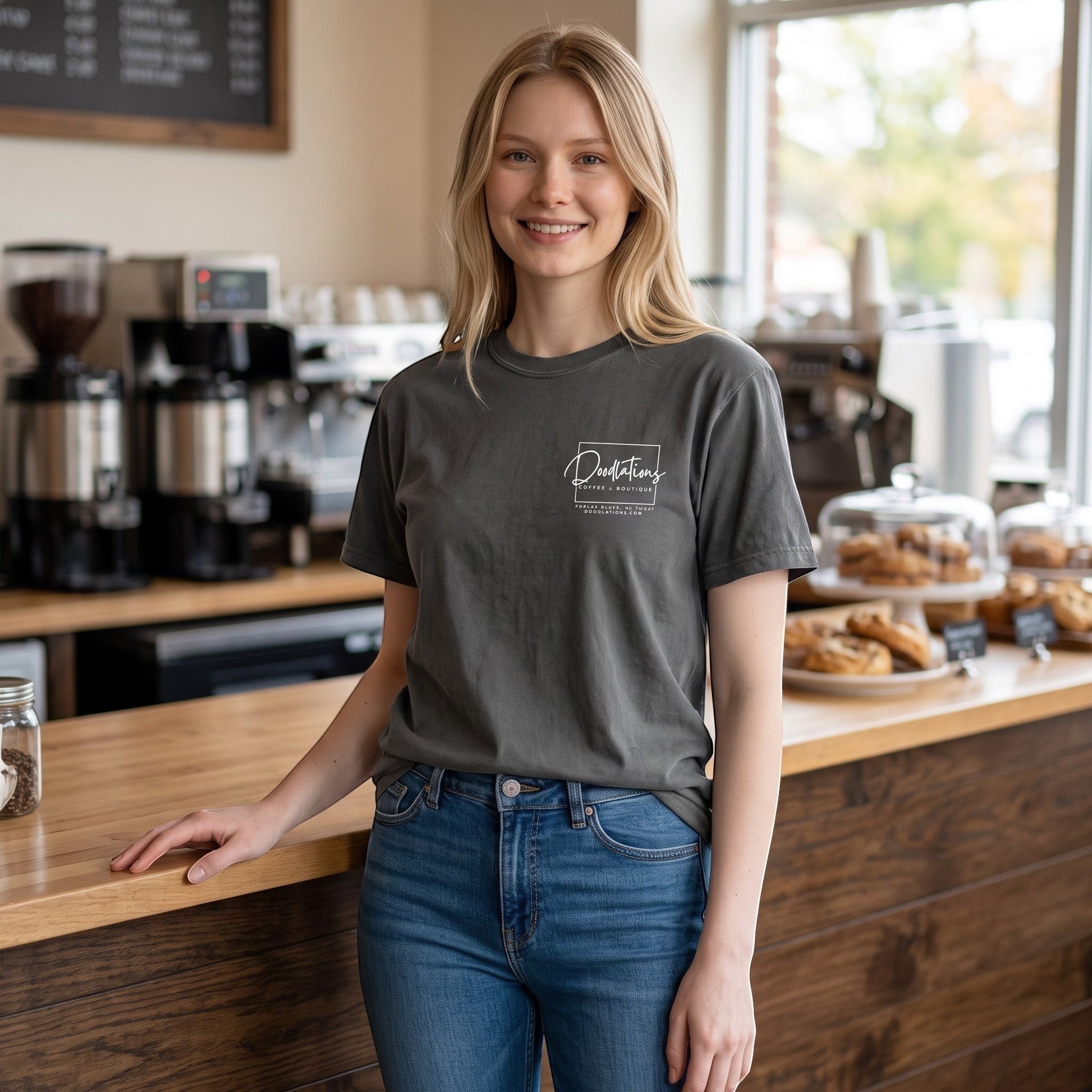 Woman wearing a charcoal grey Doodlations Coffee Bar & Boutique graphic tee with a white logo in a coffee shop