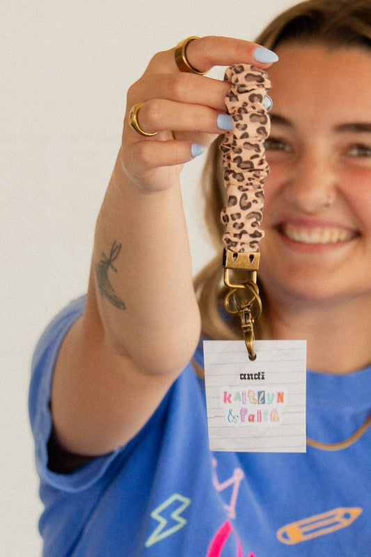Doodlations Coffee Bar & Boutique cheetah print linen scrunchie keychain held by a woman in a blue shirt