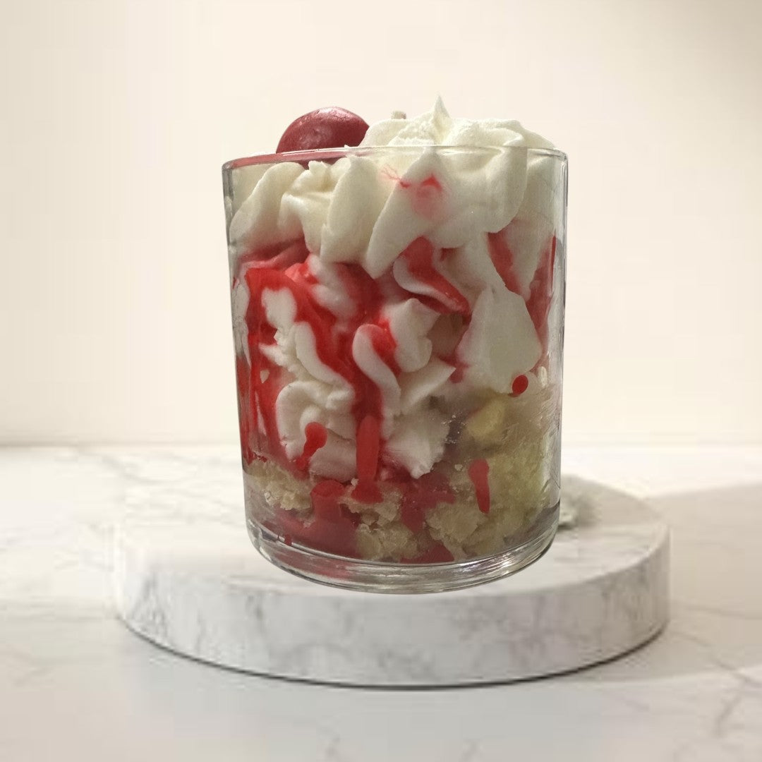 Doodlations Coffee Bar & Boutique Cherry Cheesecake candle in a glass jar, resembling dessert with white cream and red drizzle.