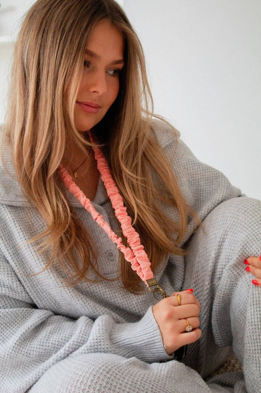 Doodlations Coffee Bar & Boutique coral gingham fabric scrunchie style lanyard worn by a woman in a grey sweater