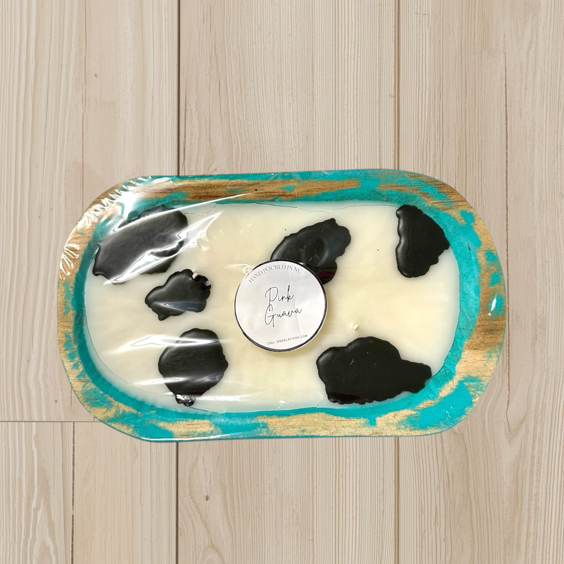 Doodlations Coffee Bar & Boutique cow dough bowl candle with pink guava scent, featuring black cow spots and a turquoise distressed wood finish.