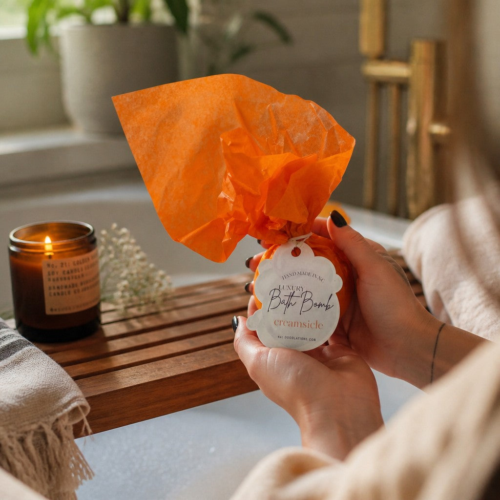 Doodlations Coffee Bar & Boutique Creamsicle bath bomb wrapped in orange tissue paper held over a warm bathtub