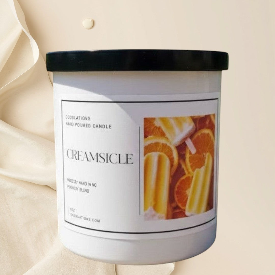 Doodlations Coffee Bar & Boutique Creamsicle hand-poured candle with vanilla and citrus scent. White jar with black lid.