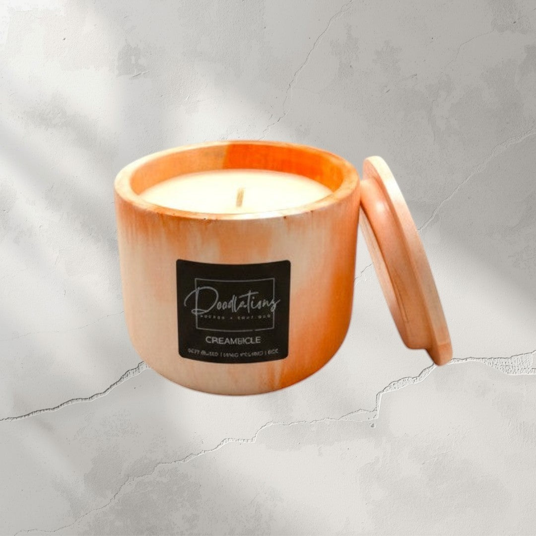 Doodlations Coffee Bar & Boutique Creamsicle marbled concrete candle with lid. Orange and white swirl design.
