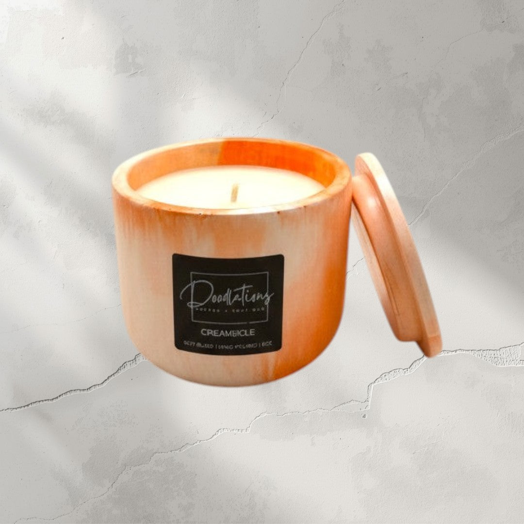 Doodlations Coffee Bar & Boutique Creamsicle marbled concrete candle with lid. Orange and white swirl design.