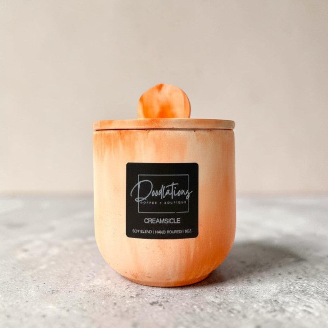 Doodlations Coffee Bar & Boutique Creamsicle concrete candle in a marbled orange and white handcrafted vessel.