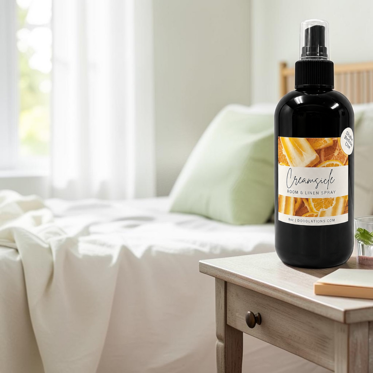 Doodlations Coffee Bar & Boutique Creamsicle room and linen spray in a black bottle on a wooden bedside table.