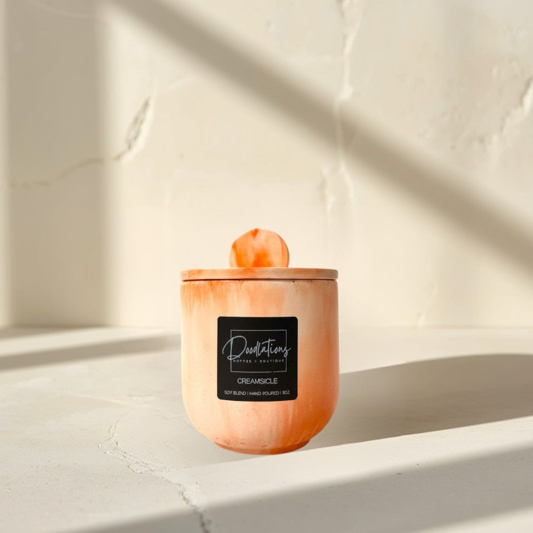 Doodlations Coffee Bar & Boutique Creamsicle marbled concrete candle with lid, orange and white swirl design.