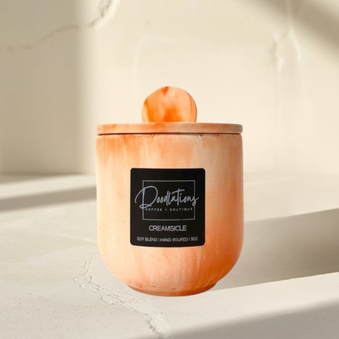 Doodlations Coffee Bar & Boutique Creamsicle marbled concrete candle with lid, orange and white swirl design.