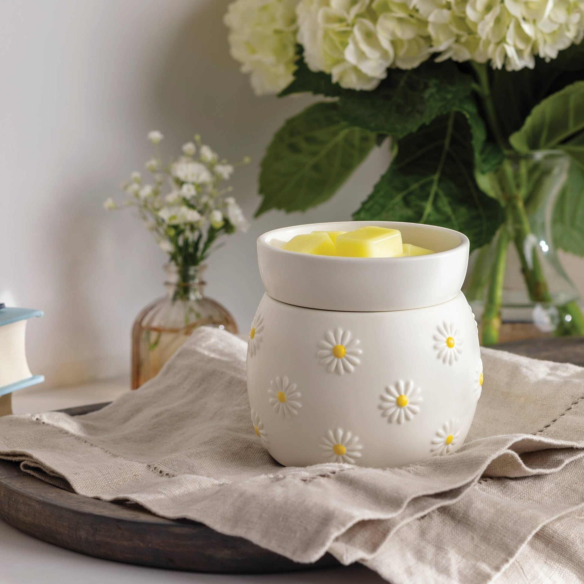 Doodlations Coffee Bar & Boutique Daisy Delight Wax Warmer, white ceramic with raised daisy design and yellow centers, filled with wax melts.
