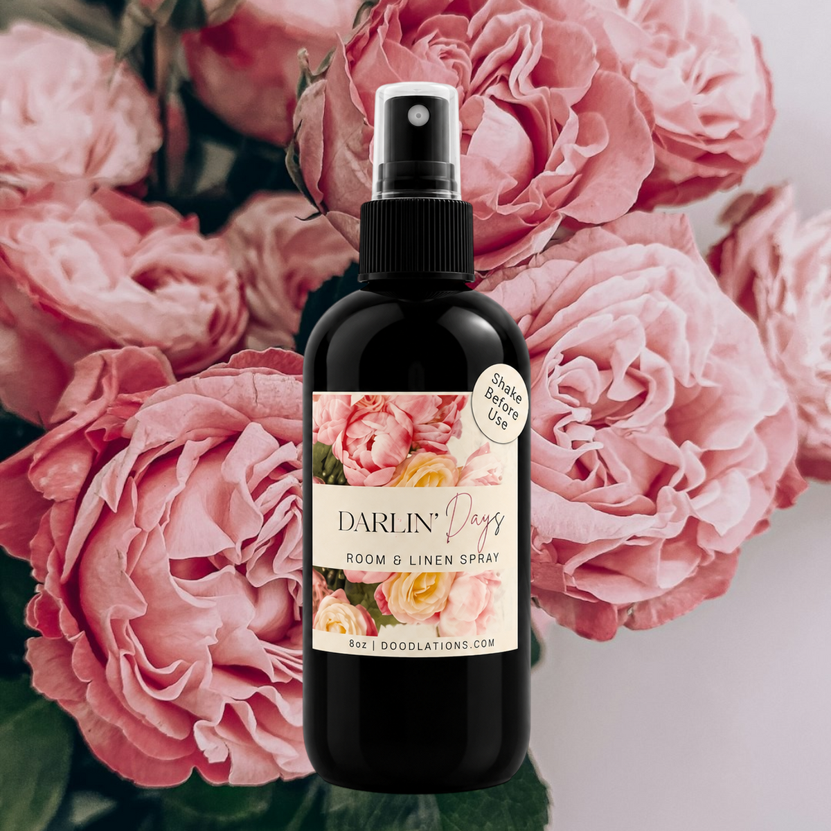 Doodlations Coffee Bar & Boutique Darlin’ Days room and linen spray in a black bottle against a backdrop of pink roses.
