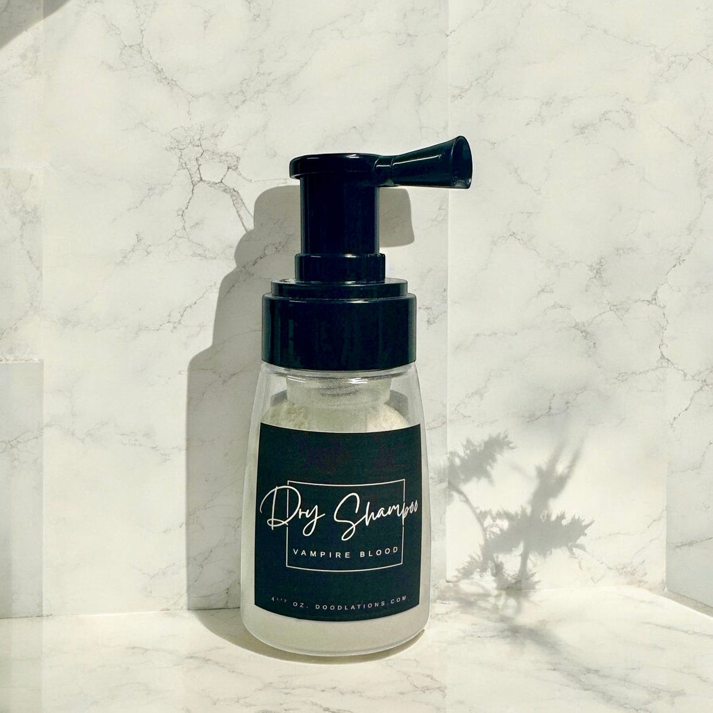 Doodlations Coffee Bar & Boutique dry powder shampoo in a clear pump bottle with a black label against a marble background