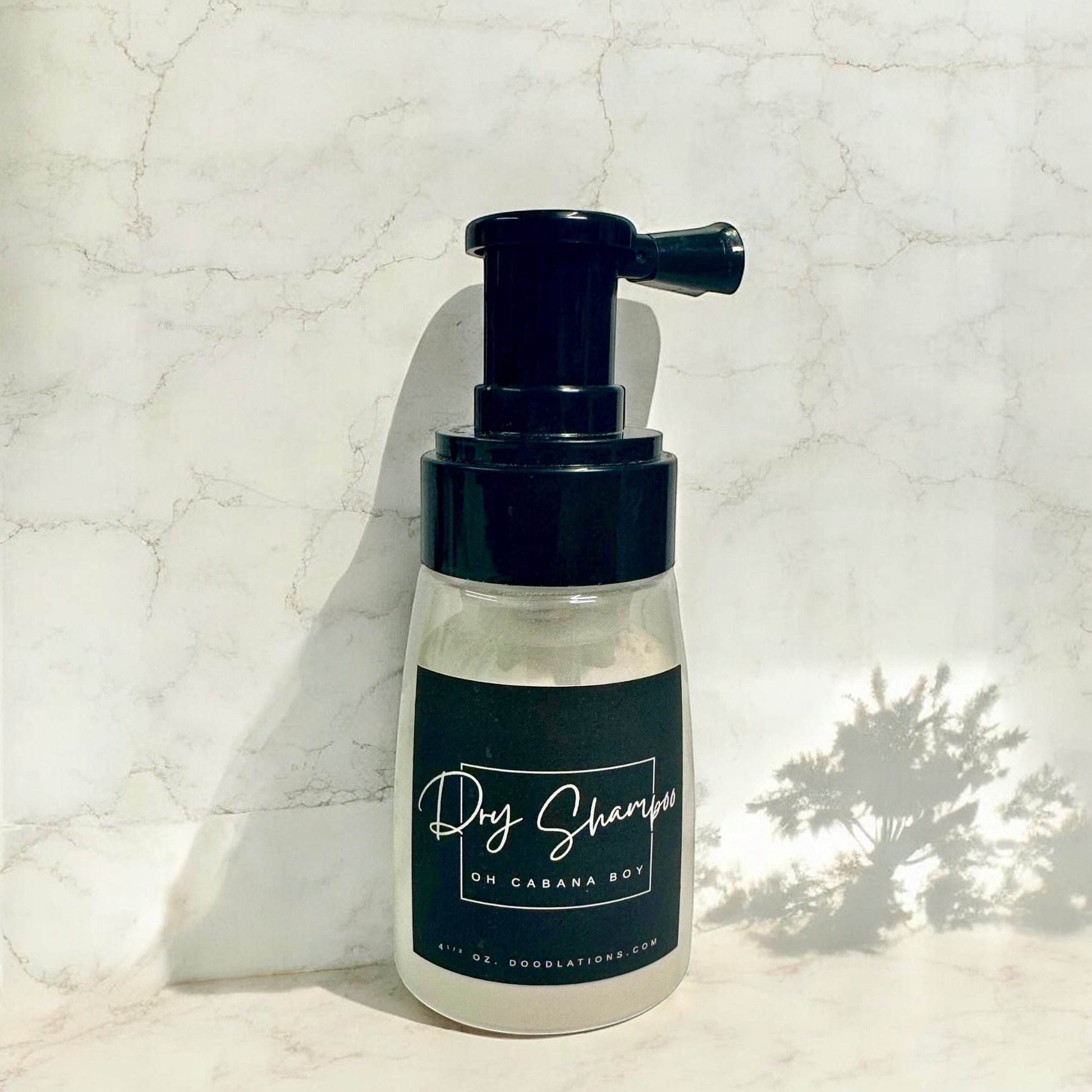Doodlations Coffee Bar & Boutique dry powder shampoo in a clear bottle with a black pump dispenser on a marble surface.
