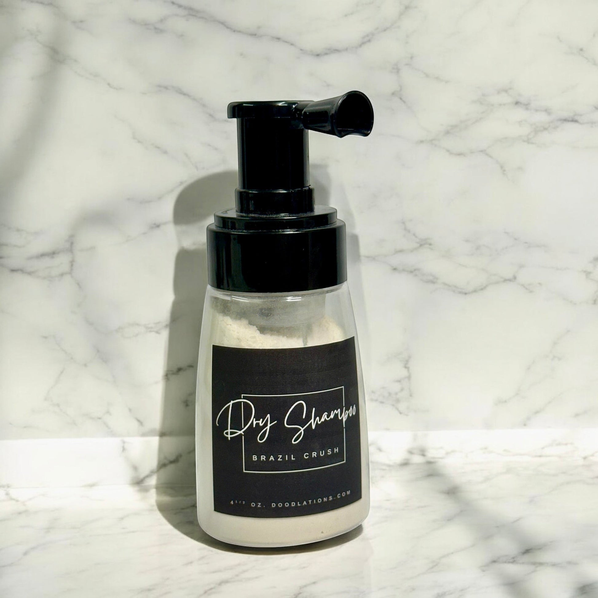 Doodlations Coffee Bar & Boutique dry powder shampoo in a clear pump bottle with a black label on a marble background.