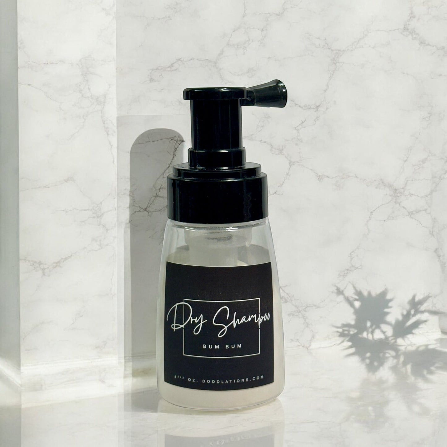 Doodlations Coffee Bar & Boutique dry powder shampoo in a clear pump bottle with a black label on a marble surface.
