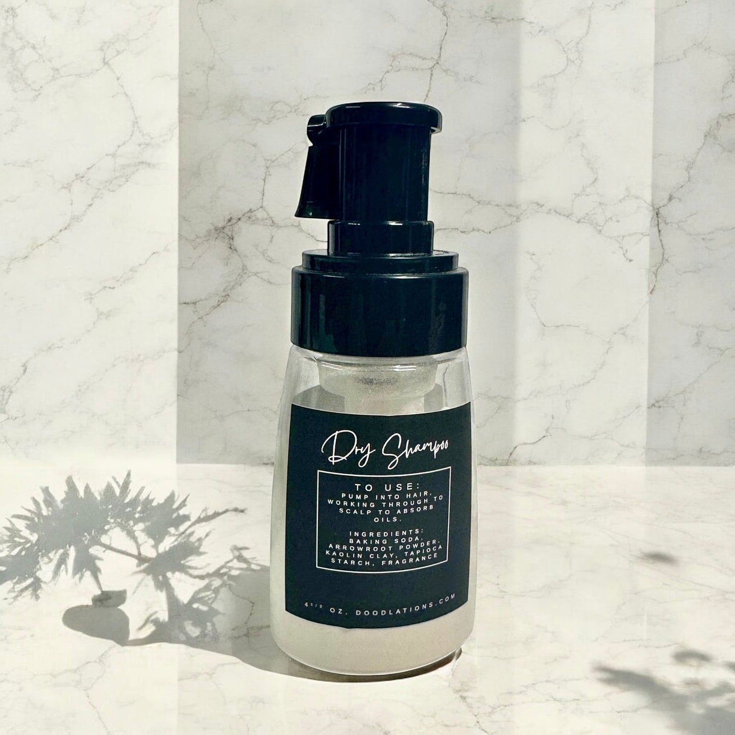 Doodlations Coffee Bar & Boutique dry powder shampoo in a clear pump bottle with a black label on marble background