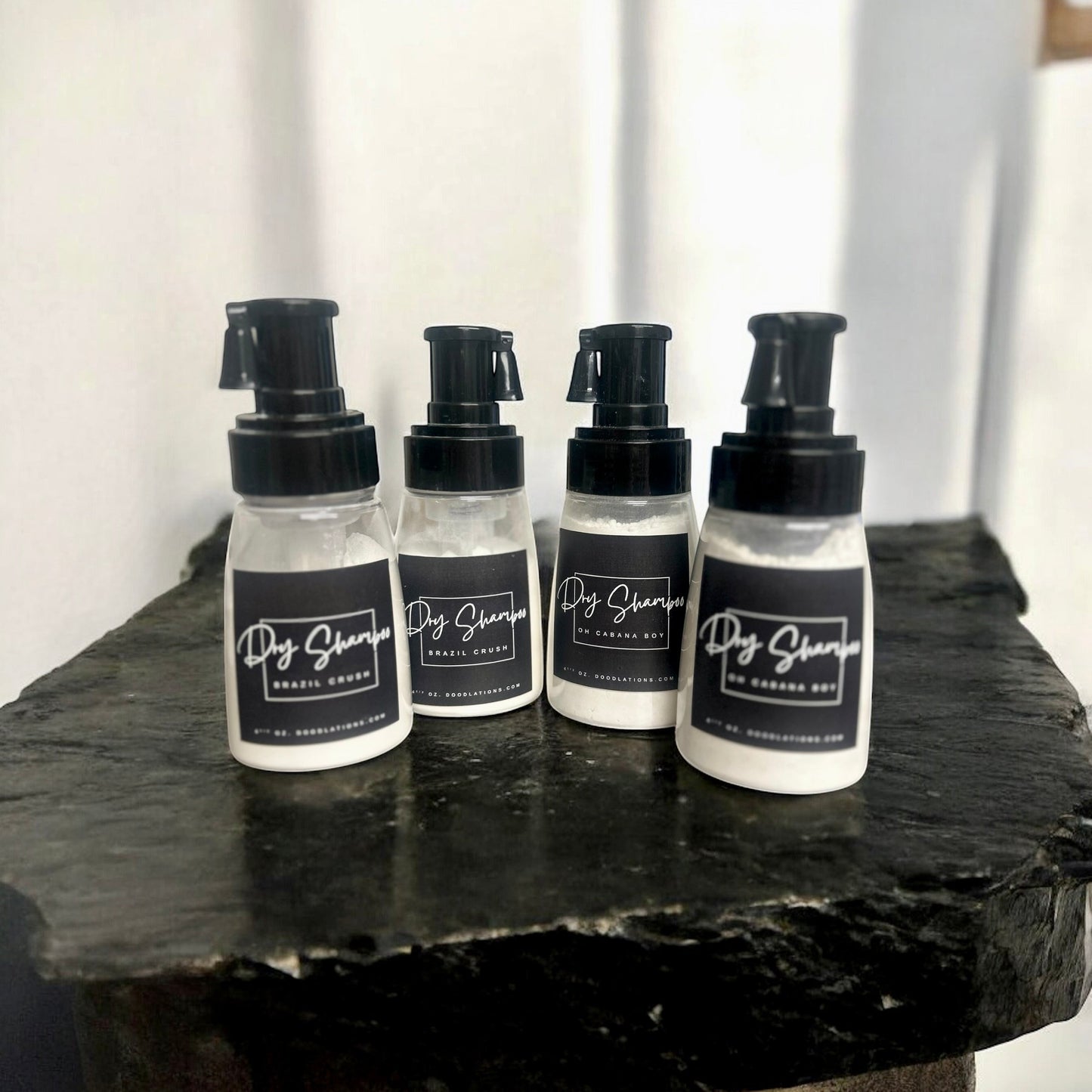 Doodlations Coffee Bar & Boutique dry powder shampoo bottles with black pump dispensers on a dark stone surface