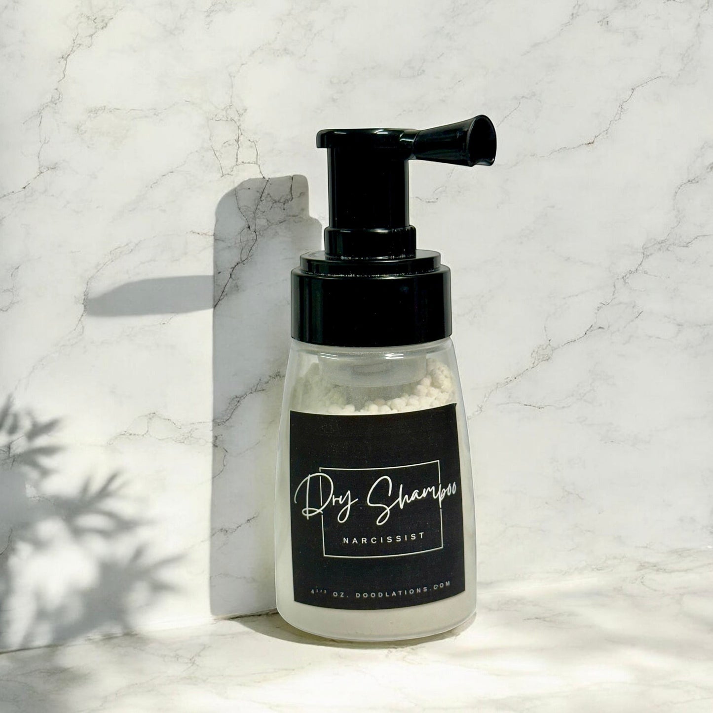 Doodlations Coffee Bar & Boutique dry powder shampoo in a clear pump bottle with a black label on a marble surface.