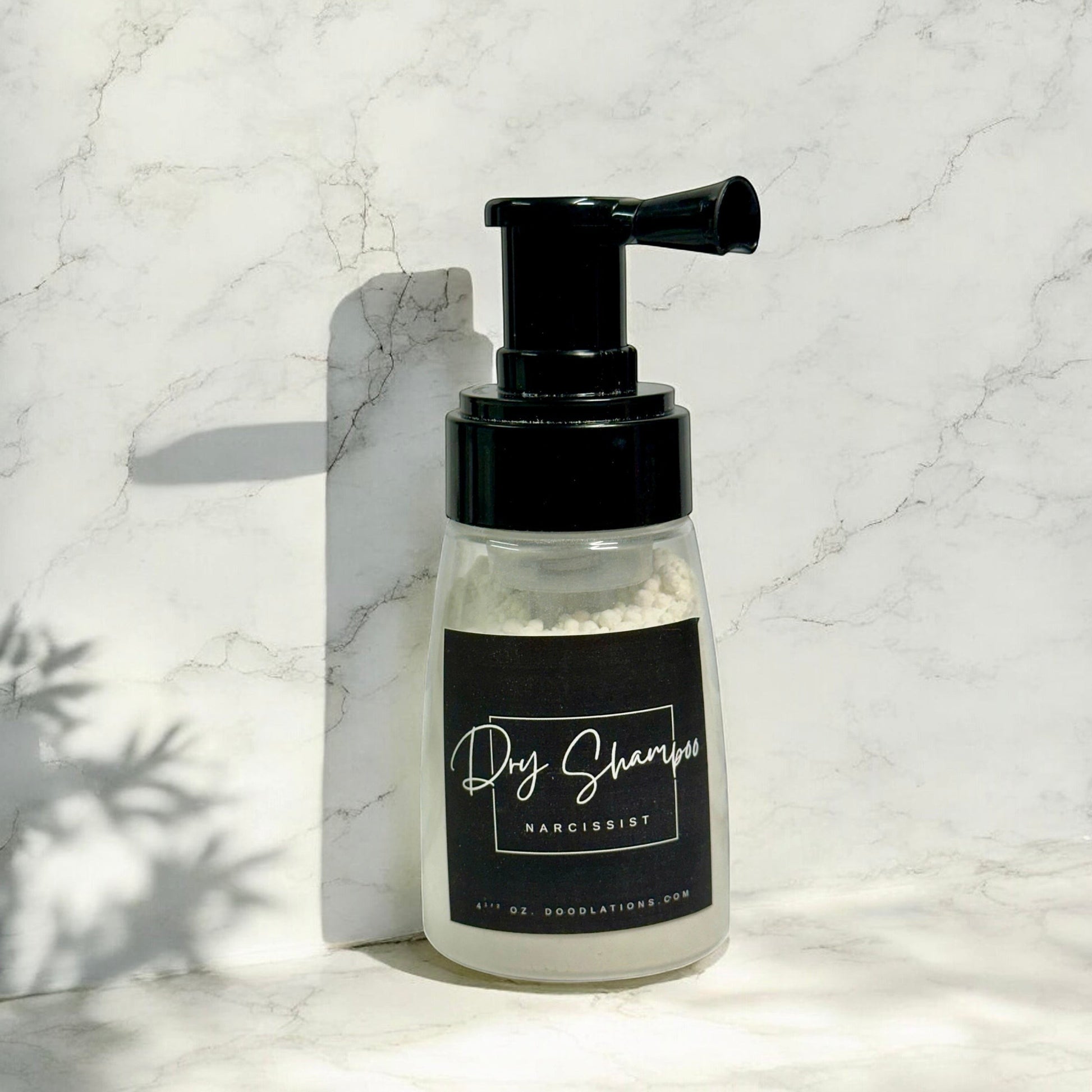 Doodlations Coffee Bar & Boutique dry powder shampoo in a clear pump bottle with a black label on a marble surface.