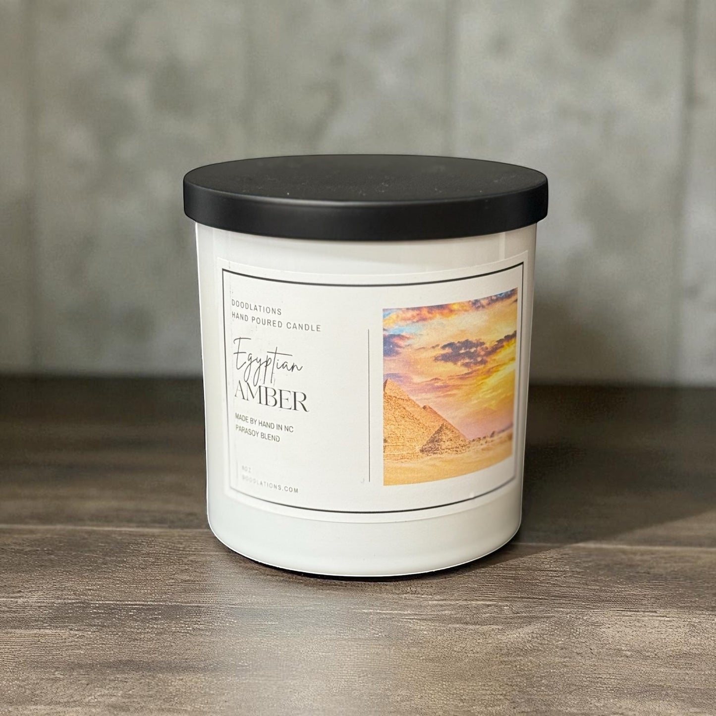Doodlations Coffee Bar & Boutique Egyptian Amber hand-poured candle in a white jar with a black lid. Features a label with pyramids at sunset.
