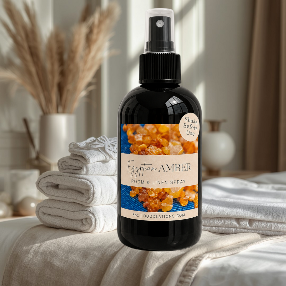 Doodlations Coffee Bar & Boutique Egyptian Amber room and linen spray in a black bottle on a bed with folded towels.