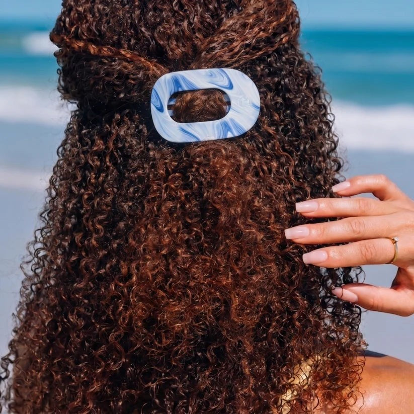 Doodlations Coffee Bar & Boutique TELETIES flat round hair clip in blue and white marble worn in curly hair at beach