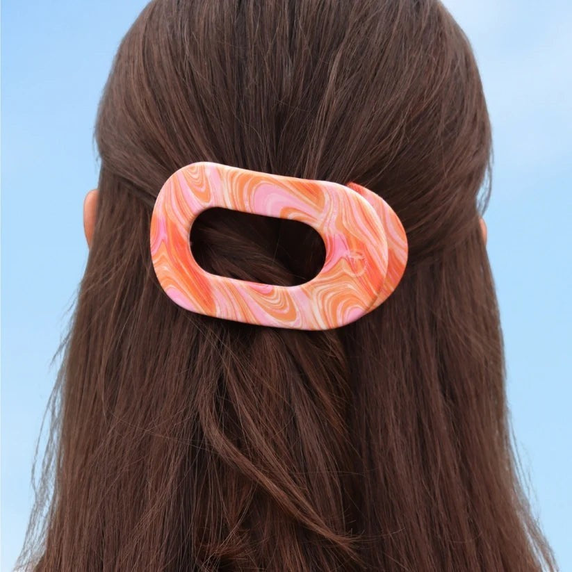Doodlations Coffee Bar & Boutique Just Keep Swimming flat round hair clip in a pink and orange marbled swirl pattern