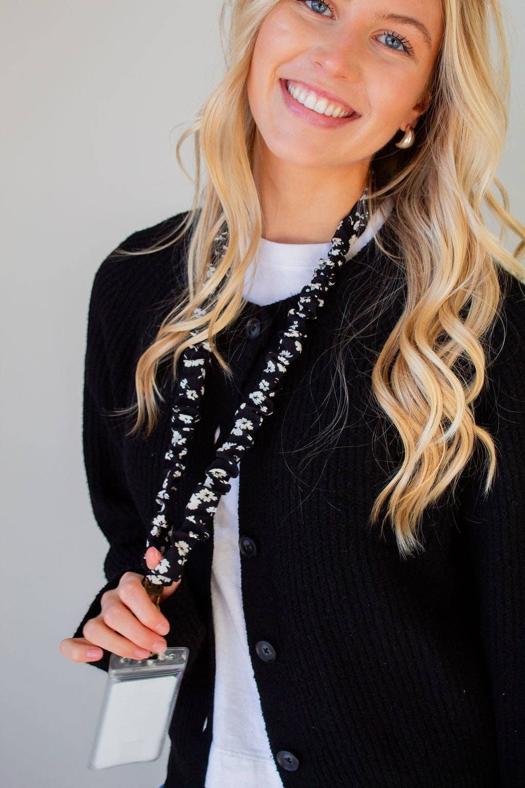 Doodlations Coffee Bar & Boutique black and white floral polyester lanyard worn by a smiling woman in a black cardigan